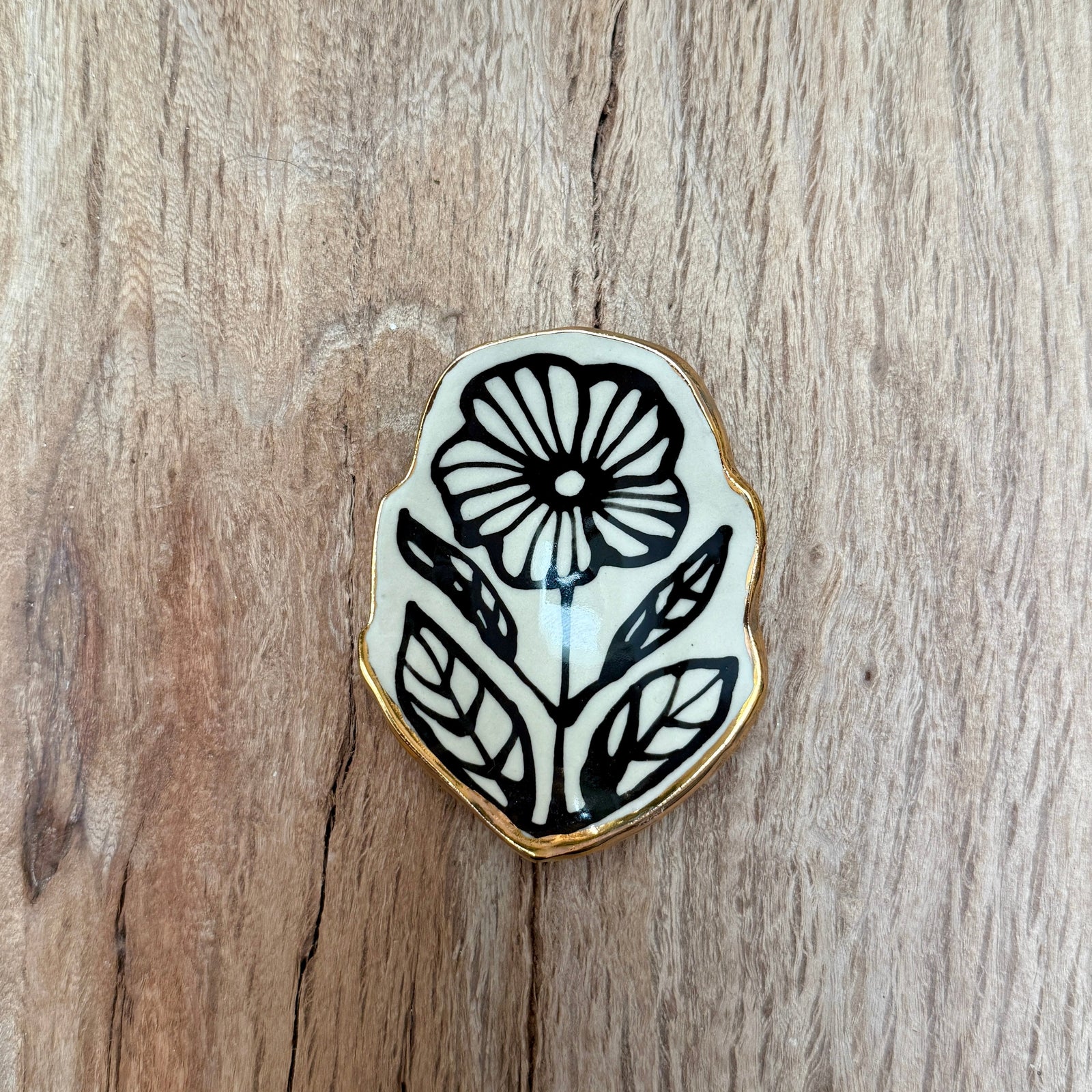A ceramic flower-shaped catchall dish with a gold edge on a wooden surface.