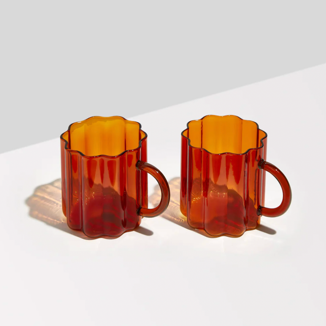 Two amber-colored glass mugs on a light gray background