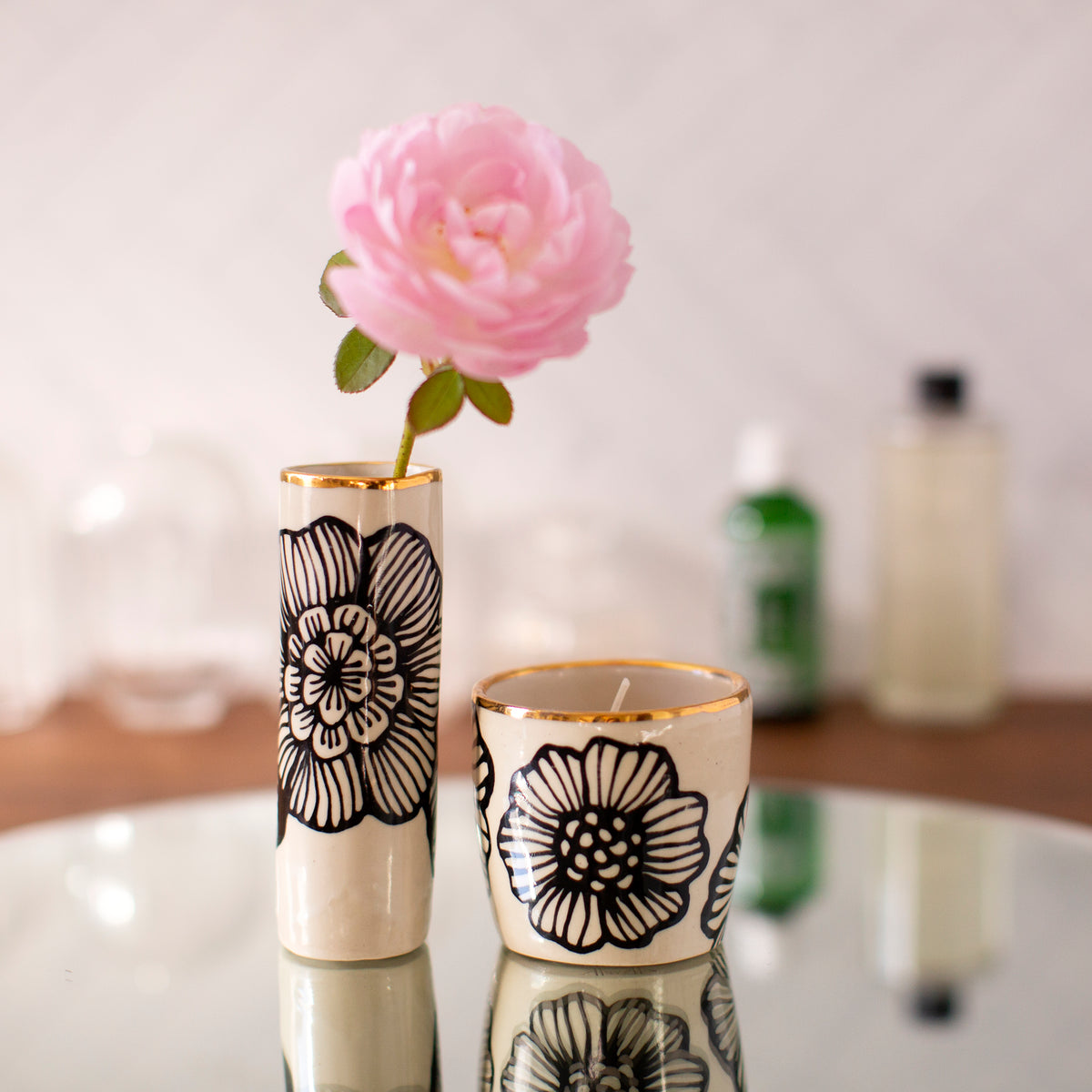 Two decorative candles with floral designs on a reflective surface.