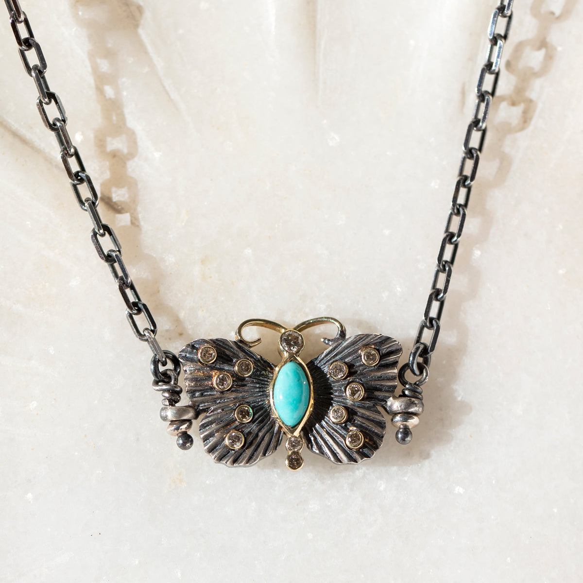 Necklace with butterfly pendant featuring a turquoise stone on a textured white background