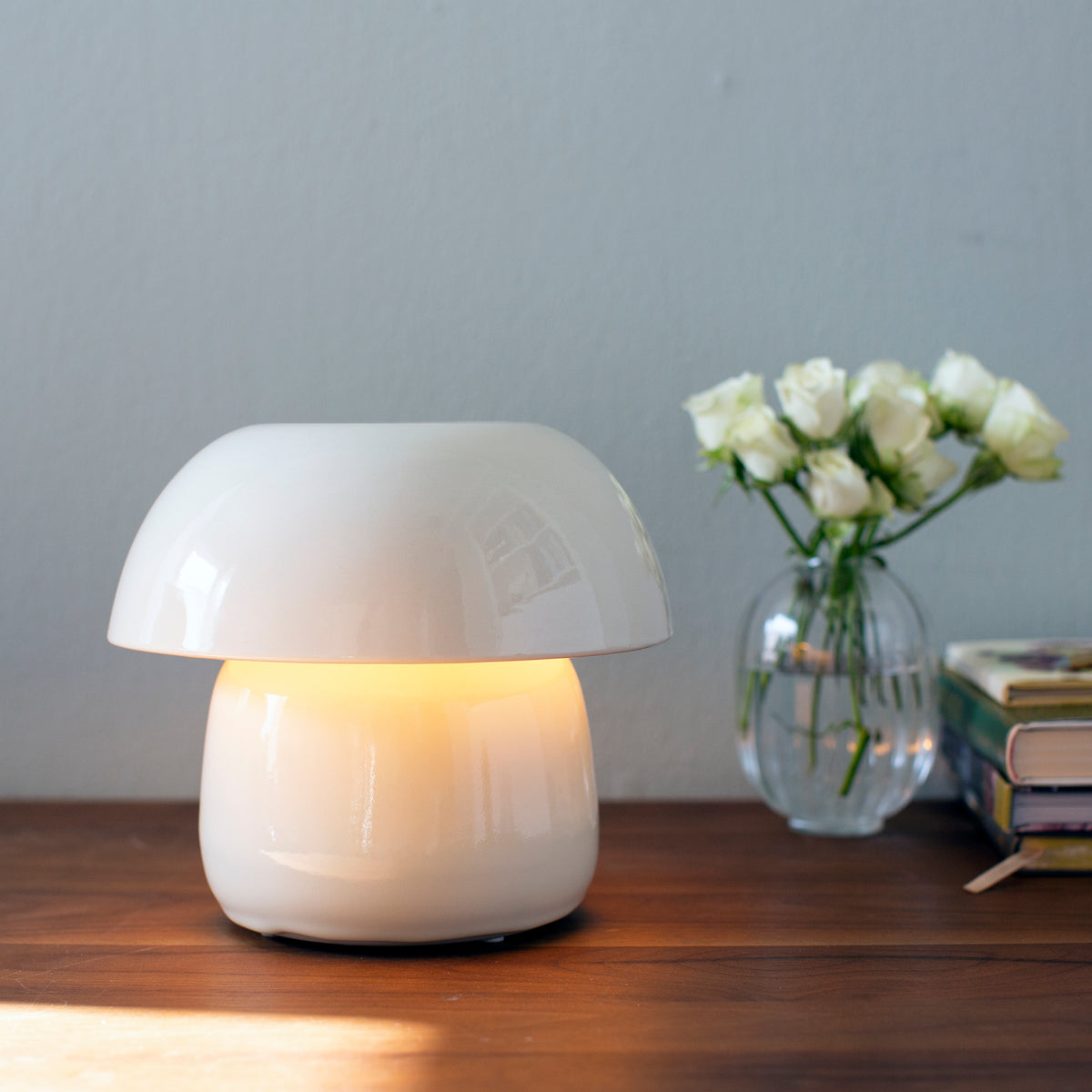 Mushroom-shaped lamp on a wooden surface with a vase of white flowers in the background.