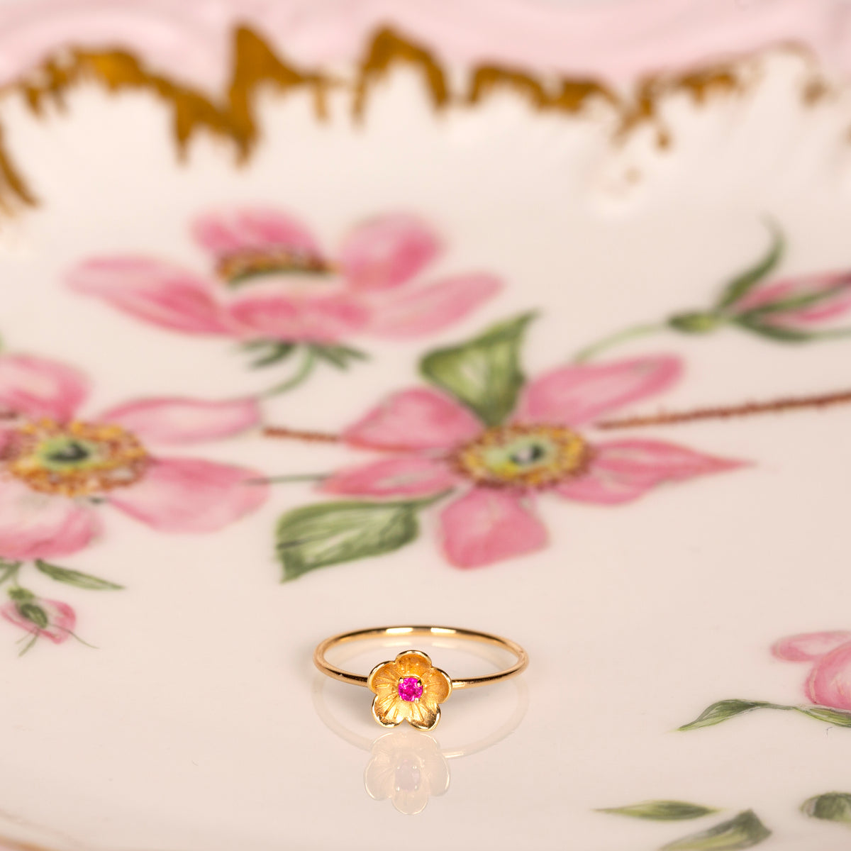 Gold ring with a pink sapphire on a floral ceramic plate